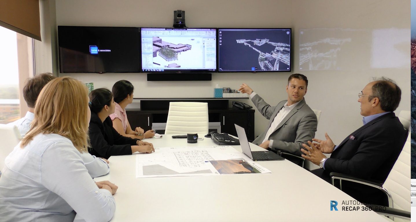 Group of architects at a conference room table discussing renderings and point clouds on a screen