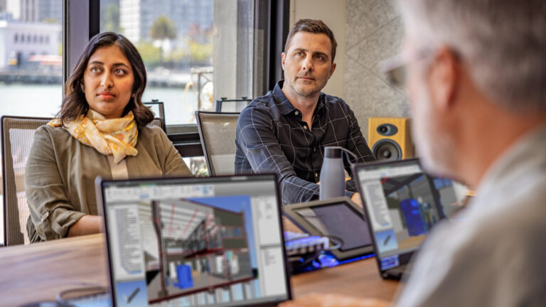 A man and a woman in a meeting with others, laptop screen on table shows use of ACC